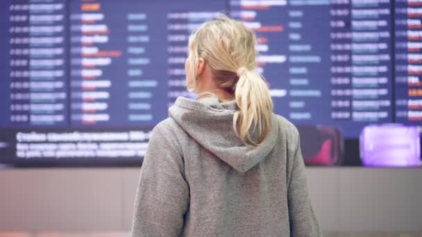Eine Passagierin am Flughafen vor dem Hintergrund der Flugpläne - Filmmaterial, Video