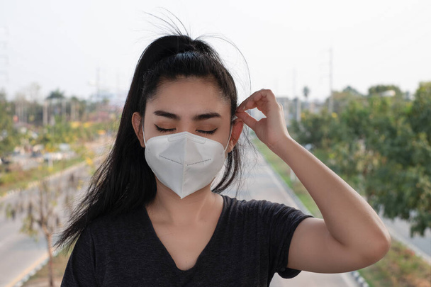 Μια γυναίκα με μαύρο πουκάμισο που στέκεται πάνω σε μάσκα του αναπνευστήρα Ν95 για να προστατευτεί από αερομεταφερόμενες αναπνευστικές παθήσεις όπως η σκόνη και το νέφος του ιού της γρίπης covid-19 coronavirus PM2.5 στο δρόμο - Φωτογραφία, εικόνα