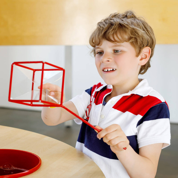 Little kid boy playing with lots of colorful plastic blocks kit in school or preschool nursery. Happy child building and creating geometric figures with soap bubbles, making experiment. - Photo, Image