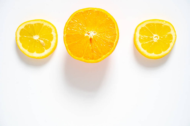 Δύο φέτες λεμόνι και μια φέτα πορτοκάλι απλωμένες στη σειρά πάνω σε λευκό φόντο. - Φωτογραφία, εικόνα