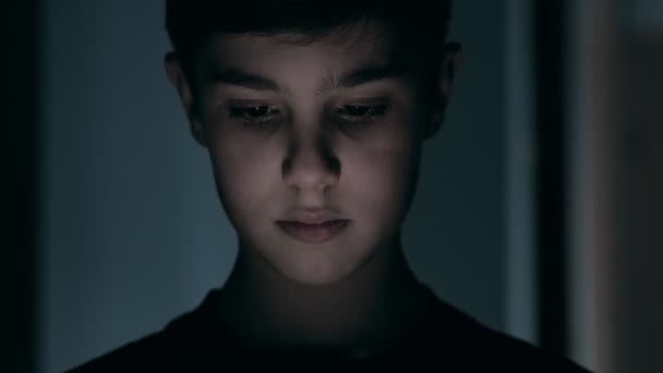 Close-up van de nacht shot van jongen van 11 leeftijden met behulp van smartphone. licht reflectie op gezicht schattig jong jongen. - Video