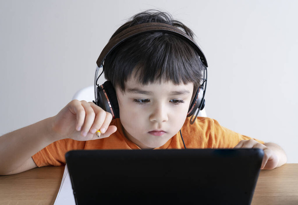 Νηπιοκόμος που χρησιμοποιεί tablet για την εργασία του, Παιδί που φοράει το κεφάλι τηλέφωνο κάνει την εργασία χρησιμοποιώντας ψηφιακή ταμπλέτα που αναζητούν πληροφορίες στο διαδίκτυο, Αρχική εκπαίδευση έννοια, Κοινωνική Αποστάσεις - Φωτογραφία, εικόνα