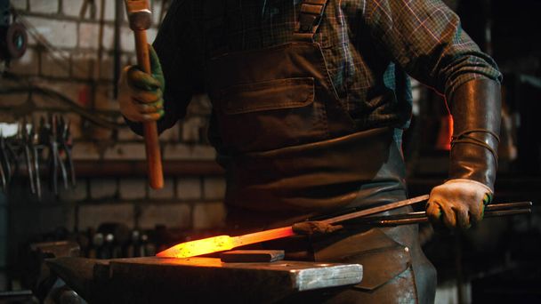Schmied arbeitet in der Werkstatt - Mann schlägt mit Hammer auf heißes Metall ein - Foto, Bild