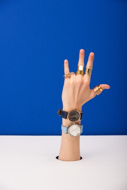 cropped view of woman with wristwatches on hand and golden rings isolated on blue - 写真・画像