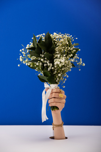 vista cortada da mulher com pulseira e anéis segurando buquê de flores da primavera isolado em azul
 - Foto, Imagem