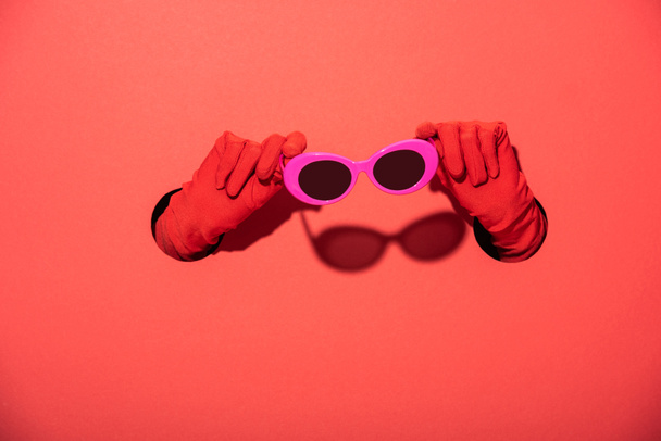 vista recortada de la mujer en guantes con gafas de sol de color rosa en rojo
 - Foto, Imagen