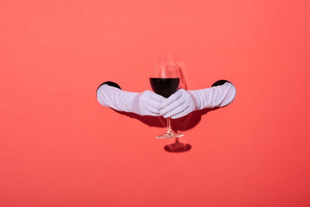 обрезанный вид женщины в перчатках с бокалом красного вина на красном
 - Фото, изображение