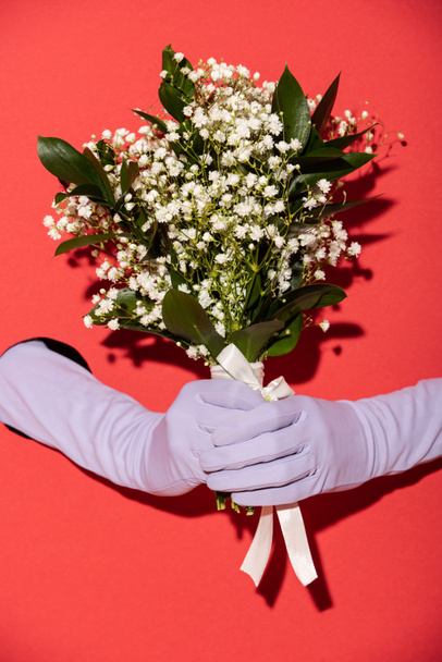 cropped view of woman in gloves holding bouquet of white spring flowers on red - Fotó, kép