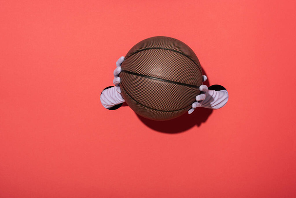 καλλιεργημένη άποψη της γυναίκας με γάντια που κρατά το μπάσκετ στο κόκκινο - Φωτογραφία, εικόνα