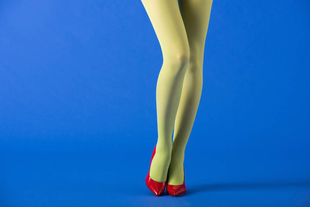 cropped view of model in green tights and red shoes standing on blue  - Fotó, kép