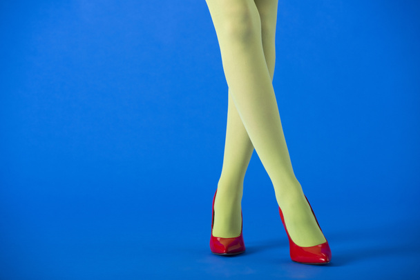 cropped view of woman in green tights and red heels posing on blue  - Photo, Image