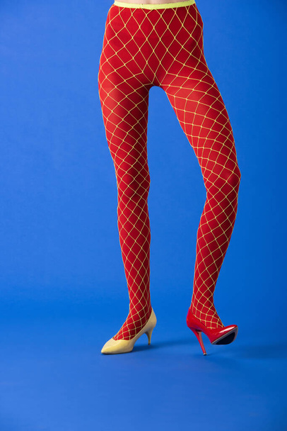 cropped view of model in fishnet tights, yellow and red heels standing on blue - Фото, изображение