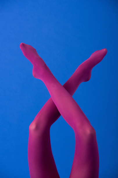 cropped view of woman in bright purple tights with crossed legs on blue - Foto, Imagen