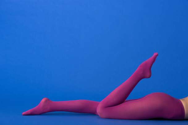 cropped view of model in trendy purple tights lying on blue - Foto, imagen