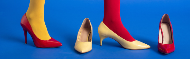 panoramatický záběr ženy v červené a žluté punčocháče a boty pózující na modré - Fotografie, Obrázek
