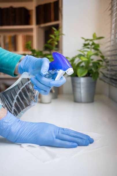 Yüzeyde ev temizliği antibakteriyel sprey sprey spreyi sıkarak COVID-19 'a karşı dezenfekte ederek mavi eldiven takarak yayılıyor. Hastanelerde ve kamusal alanlarda yüzeylerin temizlenmesi. - Fotoğraf, Görsel
