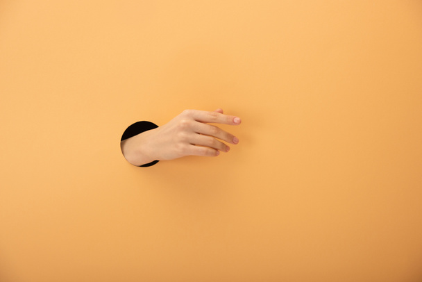 cropped view of hole with hand of woman gesturing on orange  - Fotografie, Obrázek