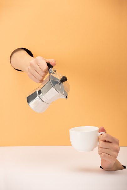cropped view of woman holding coffee pot with cup on orange and white  - Foto, afbeelding