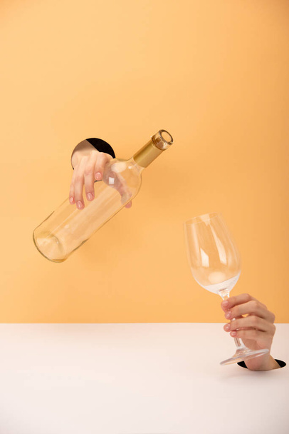 vista cortada da mulher segurando garrafa e vidro em laranja e branco
  - Foto, Imagem