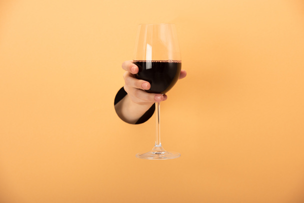 καλλιεργημένη άποψη της γυναίκας που κρατά ποτήρι κόκκινο κρασί σε πορτοκαλί  - Φωτογραφία, εικόνα