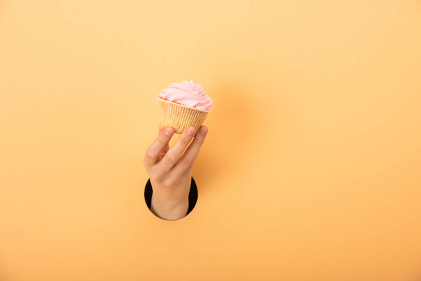 cropped view of woman holding tasty cupcake on orange - Фото, зображення