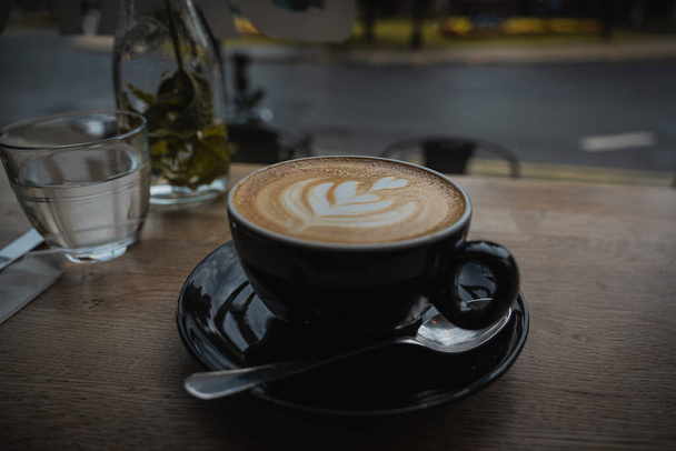 Een cappuccino koffie drinken zat op een houten rustieke tafelblad in een cafe instelling - Foto, afbeelding