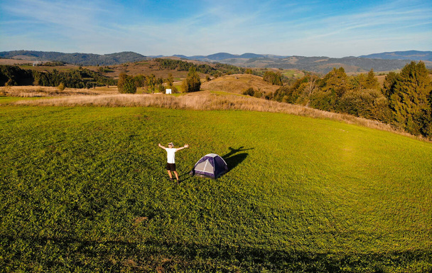 Vista aérea do homem com as mãos para cima no acampamento montanhas descansar ao pôr do sol. Liberdade
 - Foto, Imagem