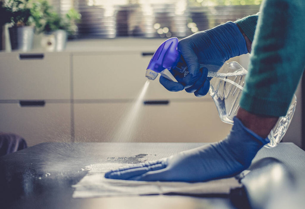 surface home cleaning spraying antibacterial sanitizing spray bottle disinfecting against COVID-19 spreading wearing medical blue gloves. Sanitize surfaces prevention in hospitals and public spaces. - Fotoğraf, Görsel
