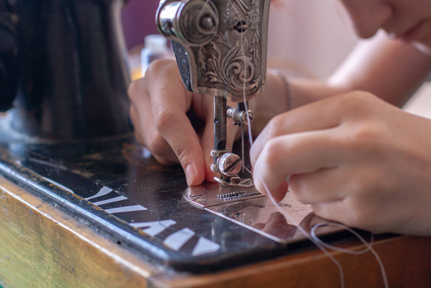 Een naaister steekt een draad in een naaldoog op een oude retro naaimachine. Focus op het oog van de naald. Horizontaal. - Foto, afbeelding