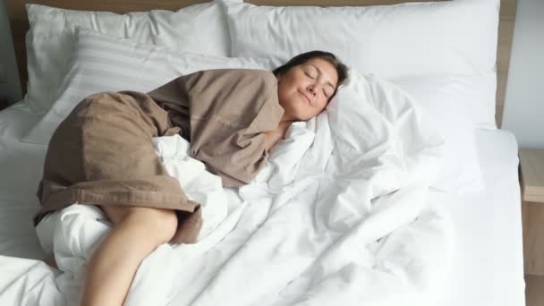 woman in bathrobe rests on soft bed with blanket and pillows - Footage, Video