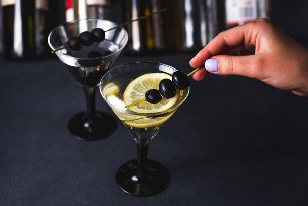 Száraz martini fekete olívabogyóval.Vermouth koktél a martini pohárban sötét háttér felett.Martini poharak vannak a pulton. szelektív fókusz - Fotó, kép