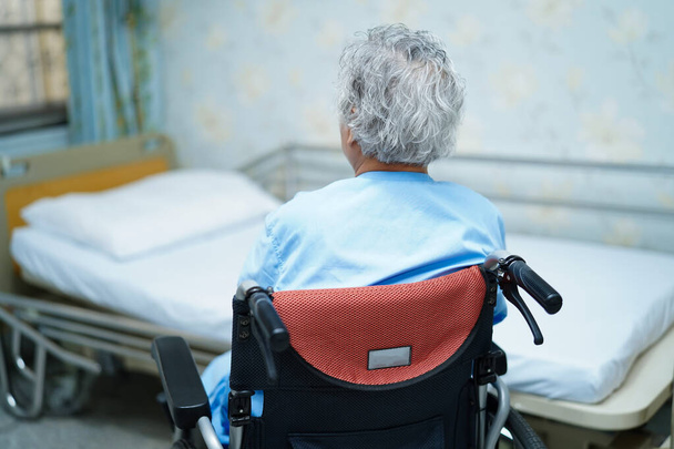 Asijské starší nebo starší stařena žena pacient sedí na invalidním vozíku v blízkosti postele v ošetřovně oddělení: zdravý silný lékařský koncept  - Fotografie, Obrázek
