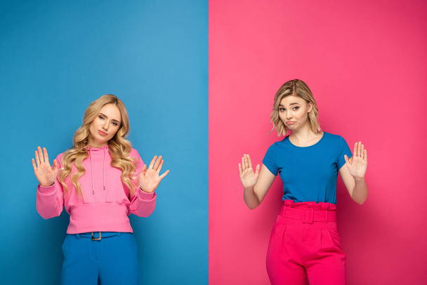 Confused blonde sisters showing stop gesture at camera on pink and blue background - Fotó, kép