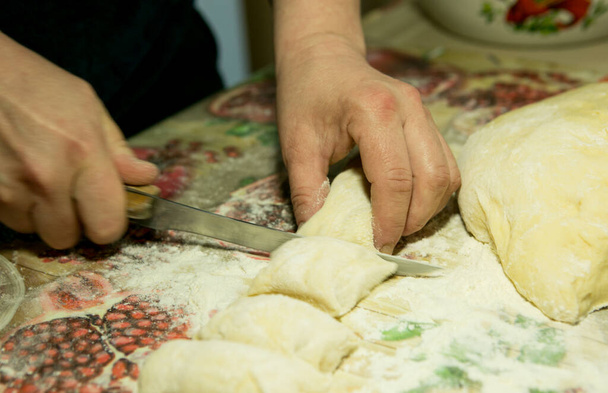Hoe tijd thuis door te brengen tijdens de periode van quarantaine en isolatie? Hobby 's voor het koken van belyashes, volgens het Oekraïense recept. Stap twee. Snijd een afgewerkt deeg met een mes voor elke belyash. - Foto, afbeelding