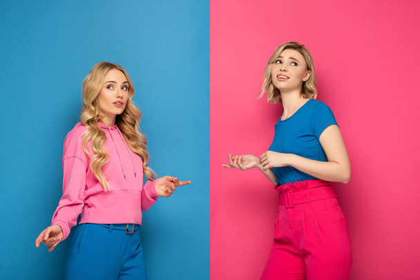 Blonde sisters pointing with fingers at each other on pink and blue background - Valokuva, kuva