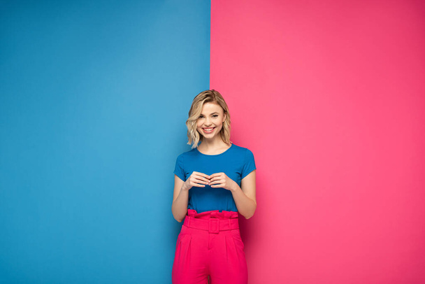 Atraktivní blondýny dívka s úsměvem na kameru na růžovém a modrém pozadí - Fotografie, Obrázek
