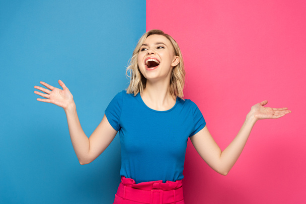 Positive blonde woman looking away on pink and blue background - 写真・画像