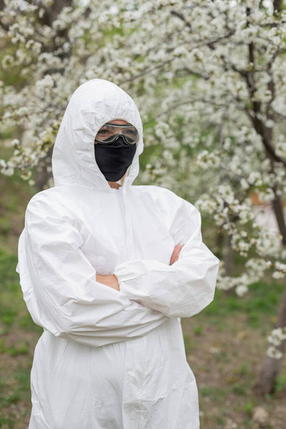 Γυναίκα με μαύρη μάσκα και λευκή προστατευτική στολή την άνοιξη - Φωτογραφία, εικόνα
