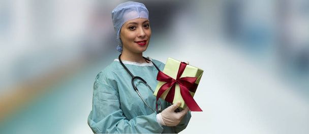 γυναίκα με προστατευτικό ιατρικό καπάκι κρατώντας κουτί δώρου στο νοσοκομείο, Χριστούγεννα έννοια - Φωτογραφία, εικόνα