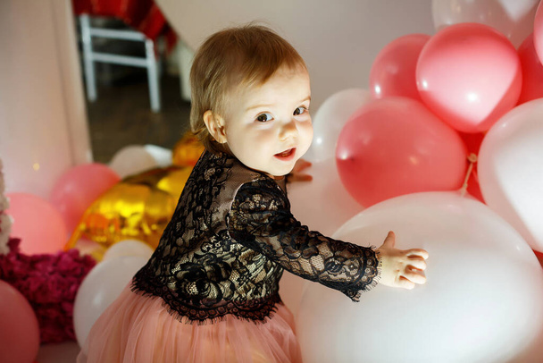 ピンクの風船でピンクのドレスを着た1歳の誕生日の女の子の写真の肖像画。休日の子供は笑顔、子供の感情。誕生日会 - 写真・画像