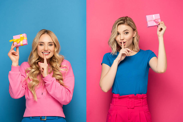 Positive blonde sisters holding gift boxes and showing silence sign on blue and pink background - Fotografie, Obrázek