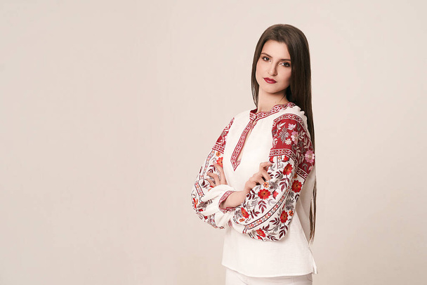 Young beautiful brunette girl wearing gorgeous ethnic style embroidered shirt, modern derivative from traditional Ukrainian vyshyvanka design. Fashion model in studio. - 写真・画像