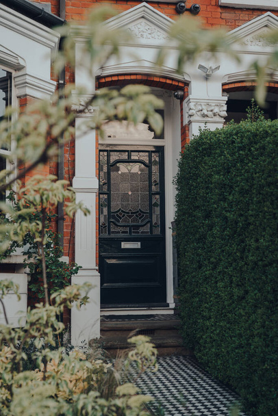 Puerta de madera de vidrieras negras de una casa eduardiana tradicional en Londres, Reino Unido, enfoque selectivo, enmarcado por árboles
. - Foto, Imagen