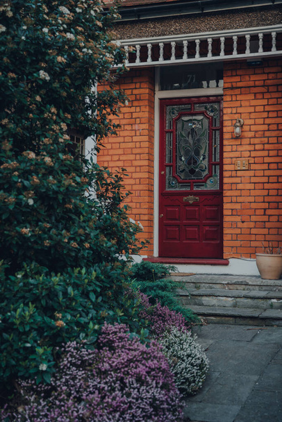 Бургундская деревянная стеклянная дверь традиционного эдвардианского дома в Лондоне, Великобритания, выборочный фокус, окруженный деревьями
. - Фото, изображение