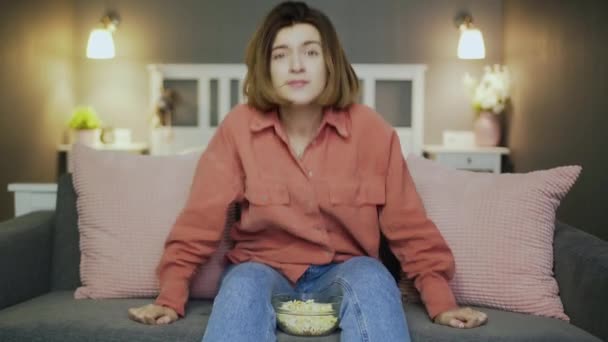 Excited woman sitting on the sofa, eating popcorn, watching football match - Materiał filmowy, wideo