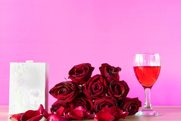 Masada kırmızı güller ve kırmızı şarap kadehi, masada hediye kutusu., - Fotoğraf, Görsel