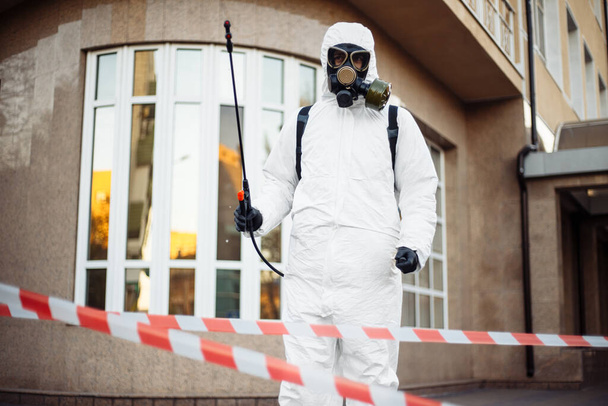 A vírusvédőt viselő egészségügyi dolgozó a vörös és fehér szalag mögött áll egy fertőtlenítő spray-vel a kezében és a hátizsákjában. Coronavirus covid-19 megelőzés - Fotó, kép
