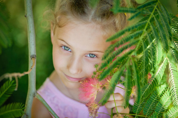 Close-up portrait of a child. Summer funny little girl next to a pink acacia in bloom. Albizia julibrissin - Photo, Image