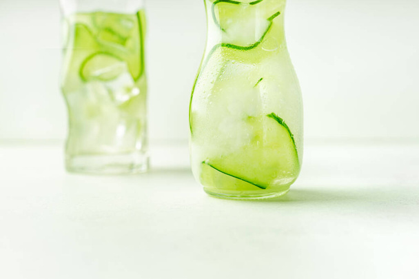 Komkommer doordrenkt water in glazen pot en highball glas, close-up uitzicht, met kopieerruimte. Horizontale oriëntatie - Foto, afbeelding