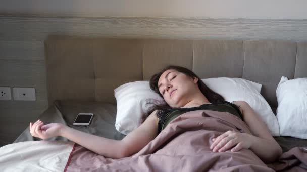 woman looks at smartphone awakening in large bed in hotel - Footage, Video